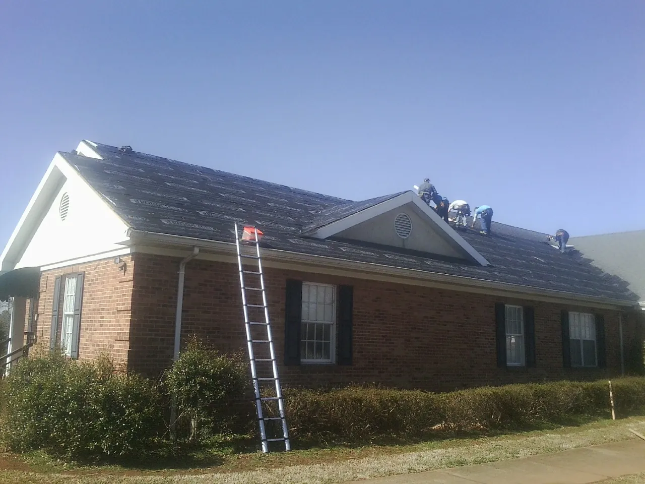 Crew tearing shingles off a brick ranch roof with a ladder set — Metal Roof Repair work by our crew in Dickerson Run