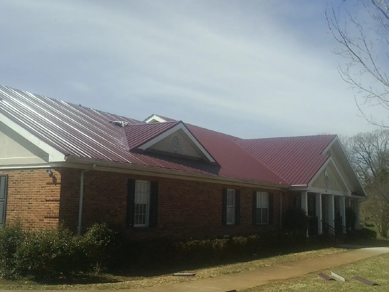 Red metal roof with gabled entries on a long brick building, from a Hail Damage Roof Repair job in Dickerson Run