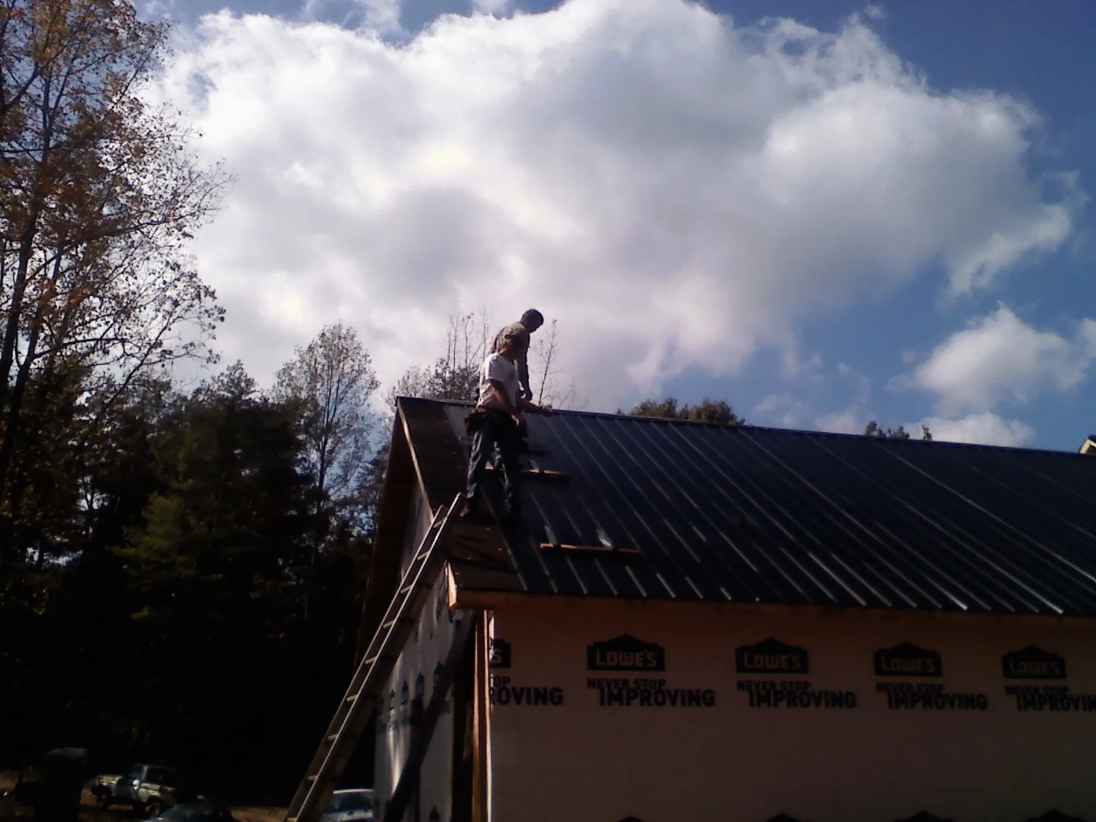 Roofer fastening dark metal panels high against a cloudy sky, from a Roof Inspection job in Dickerson Run