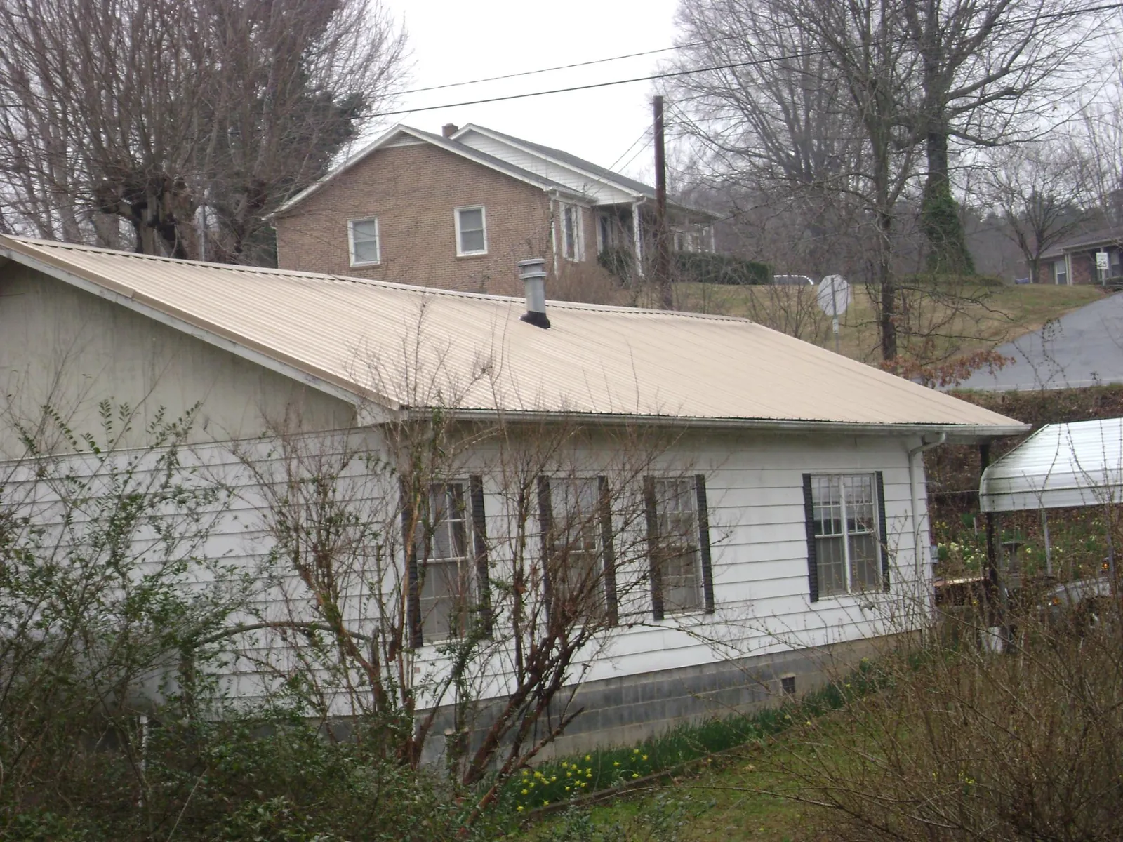 Tan metal roof on a white sided house set into a hillside — Commercial Roofing by Roofing Brothers in Dickerson Run